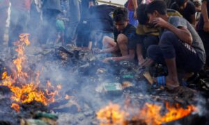 فلسطينيون يبحثون عن الطعام بين الأنقاض المحترقة بعد غارة إسرائيلية على منطقة للنازحين في رفح جنوبي غزة- 27 من أيار 2024 (رويترز)