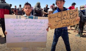 طفلان يحملان لافتات خلال وقفة احتجاجية داخل مخيم الركبان شرقي محافظة حمص شرقي سوريا- 25 من أيار 2024 (hesar)