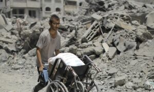 شاب فلسطيني يسير بين ركام المباني التي دمرها القصف الإسرائيلي في غزة، وينقل كيسًا من الطحين على كرسي مخصص لذوي الإعاقة، في ظل إغلاق معبر رفح بعد سيطرة الاحتلال الإسرائيلي على الجانب الفلسطيني منه- 31 من حزيران 2024 (أونروا/ إكس)