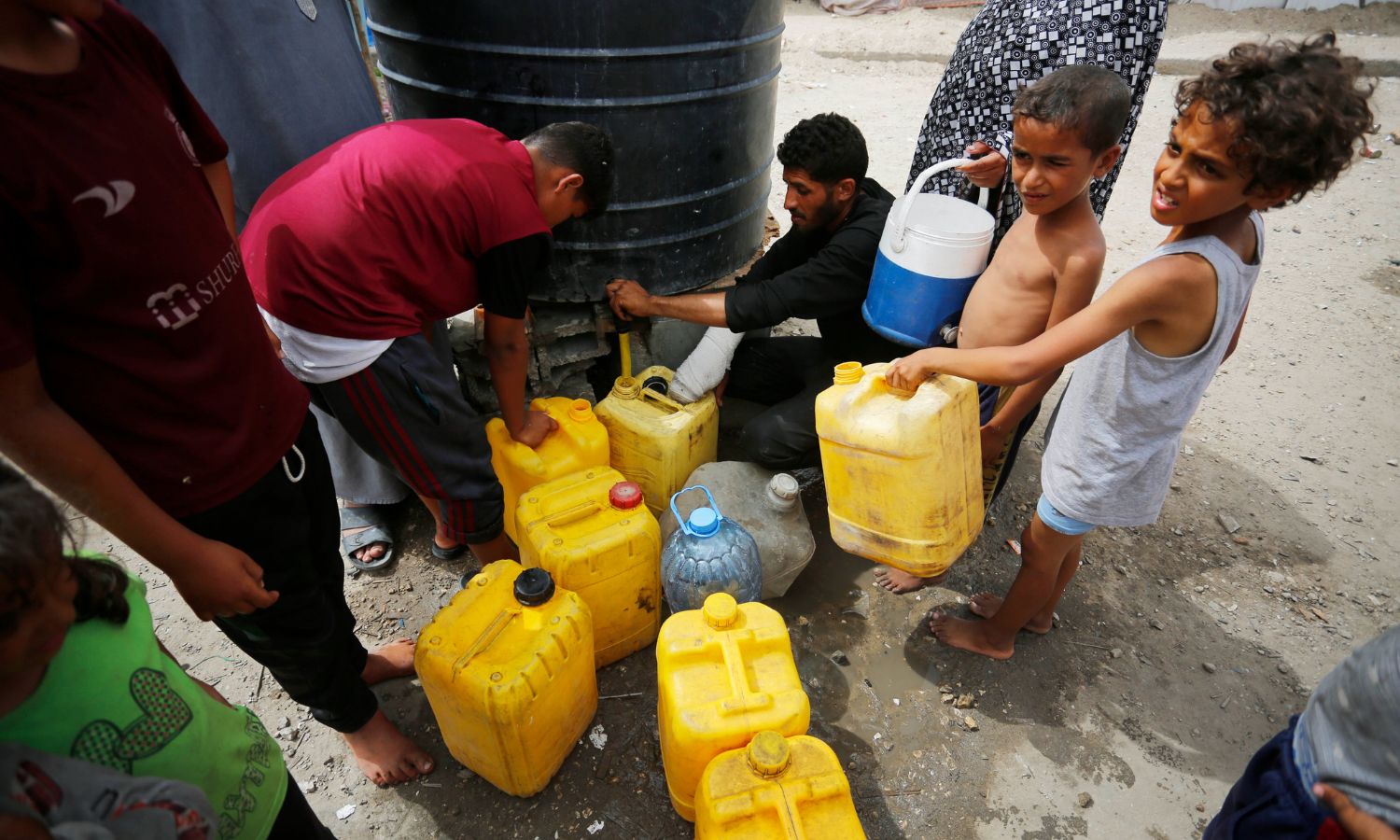 أطفال في غزة يملأون عبوات من المياه في ظل النقص الحاد في الاحتياجات الإنسانية ضمن القطاع المحاصر وبسبب مواصلة الحرب الإسرائيلية على غزة- 12 من حزيران 2024 (أونروا)