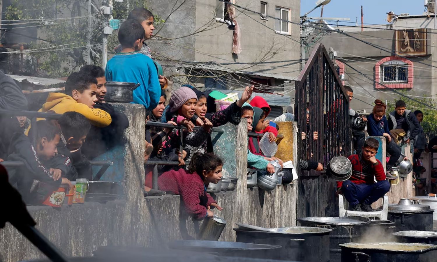 أطفال فلسطينيون في رفح، جنوبي غزة، ينتظرون الحصول على الطعام المطبوخ في مطبخ خيري وسط نقص الإمدادات الغذائية مع استمرار الحرب على غزة- 20 من شباط 2024 (رويترز)