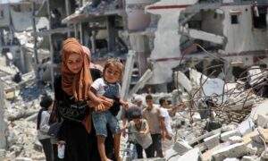 سيّدة فلسطينية تحتضن ابنتها خلال سيرها بين أنقاض المنازل المدمرة ف خان يونس، جراء الحرب الإسرائيلية على غزة- 26 من تموز 2024 (رويترز)