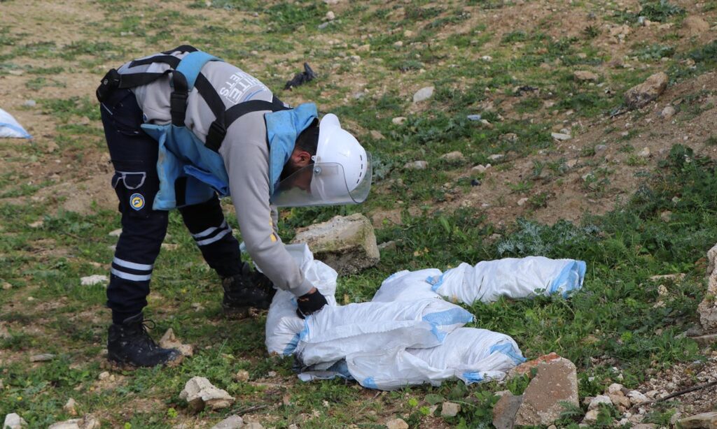 عنصر في فرق إزالة الألغام التابعة للدفاع المدني سوريا وهو يتلف مقذوف من مخلفات قصف سابق - 3 آذار 2024 (الدفاع المدني السوري/ فيس بوك)