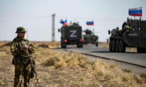 قوافل عسكرية روسية تعبر أمام جندي أمريكي في مدينة الحسكة شمال شرقي سويا 2022 (AFP)

