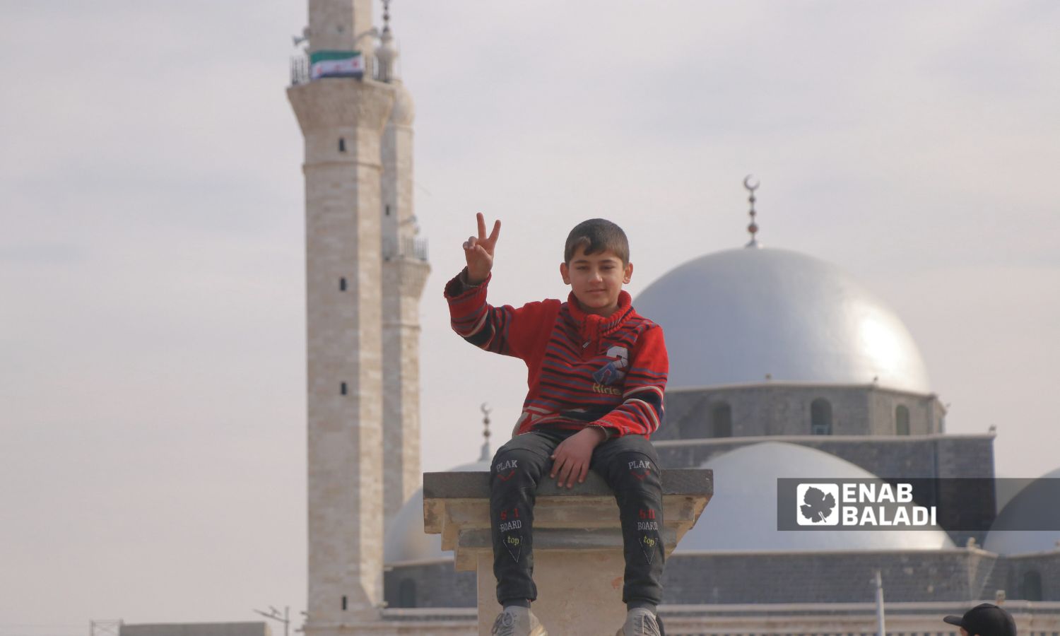 طفل يجلس أمام مسجد خالد أبن الوليد في مدينة حمص - 09 كانون الأول 2024 (عنب بلدي/ وليد الإدلبي)