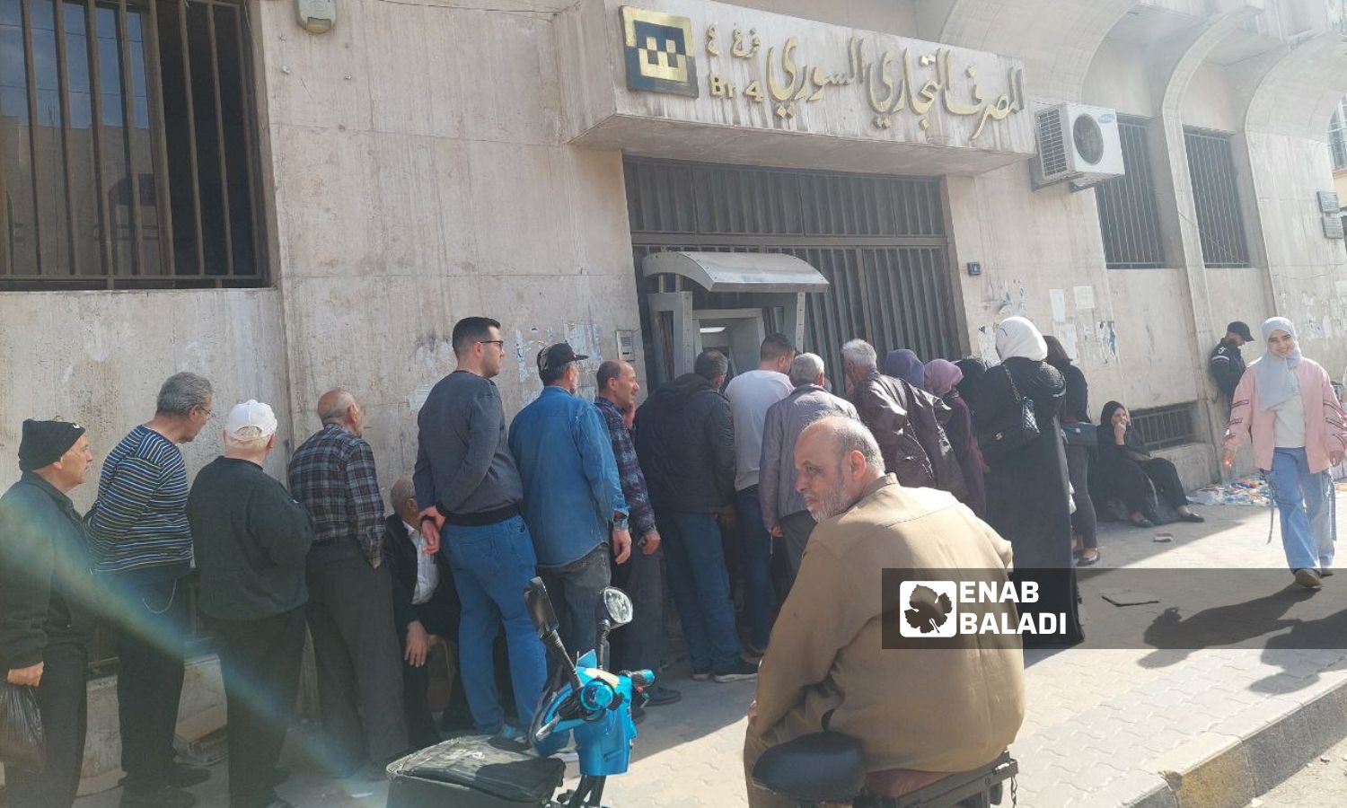 موظفون حكوميون يقفون في طابور أمام المصرف التجاري السوري بانتظار تسلم رواتبهم وسط مدينة حمص- 27 من آذار 2025 (عنب بلدي/ جنى العيسى)