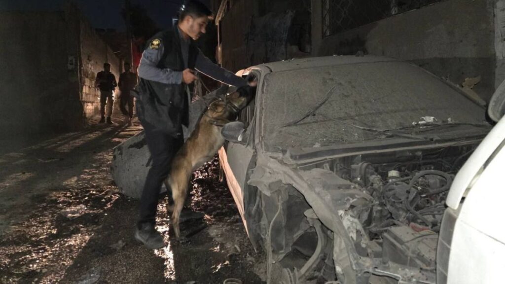 أحد عناصر قوى الأمن الداخلي يفتش سيارة متوقفة قرب مكان إنفجار عبوة ناسفة بمدخل حي المزة 86 بدمشق باستخدام الكلاب البوليسية k9، 3 أيلول 2025 (تلغرام)