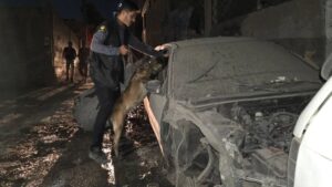 أحد عناصر قوى الأمن الداخلي يفتش سيارة متوقفة قرب مكان إنفجار عبوة ناسفة بمدخل حي المزة 86 بدمشق باستخدام الكلاب البوليسية k9، 3 أيلول 2025 (تلغرام)
