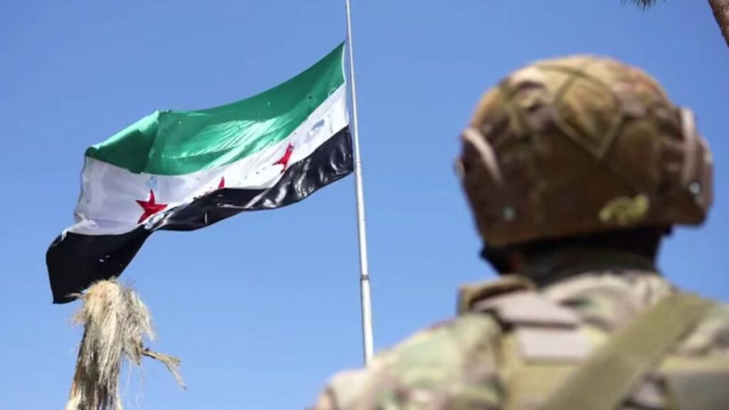 مقاتل من وزارة الدفاع ينظر إلى علم سوري ممزق جراء القصف الإسرائيلي على وزارة الدفاع 23 من تموز 2025 (وزارة الدفاع السورية)