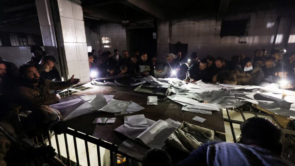أشخاص يبحثون في أوراق أثناء انضمامهم إلى أعضاء مجموعة الدفاع المدني السوري للبحث عن سجناء تحت الأرض في سجن صيدنايا - 9 كانون الأول 2024 (رويترز/ عمرو عبد الله دلش)