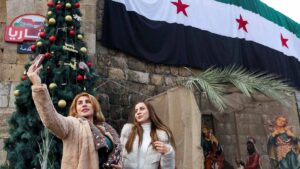 نساء يستخدمن هواتفهن المحمولة أمام علم في ساحة باب توما ليلة رأس السنة 31 كانون الأول 2024 (رويترز)
