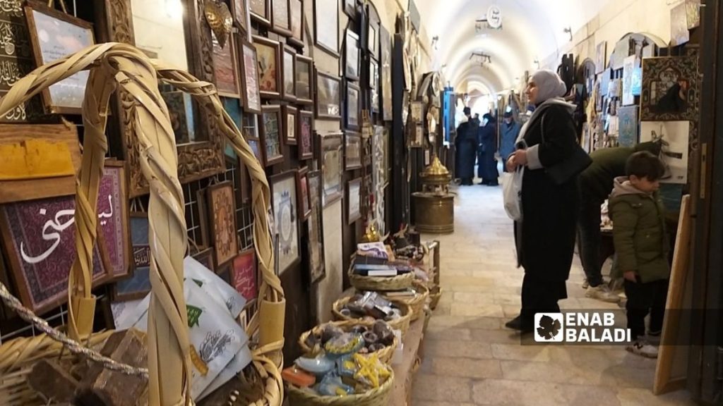 سيدة تنظر إلى رسومات معلقة على الجدران الخارجية لمحال تجارية بسوق الحبال بحلب القديمة - 21 كانون الثاني 2026 (عنب بلدي)
