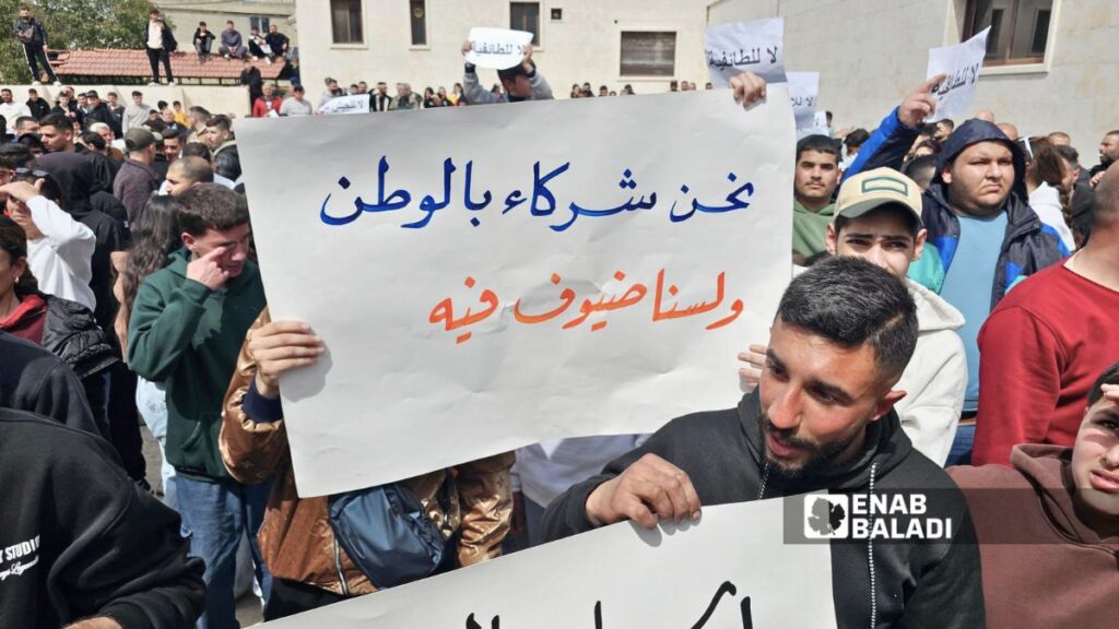 متظاهرون في السقيلبية يحملون لافتة تقول: “نحن شركاء بالوطن ولسنا ضيوفًا فيه” - 28 آذار 2026 (عنب بلدي/ إياد عبد الجواد)