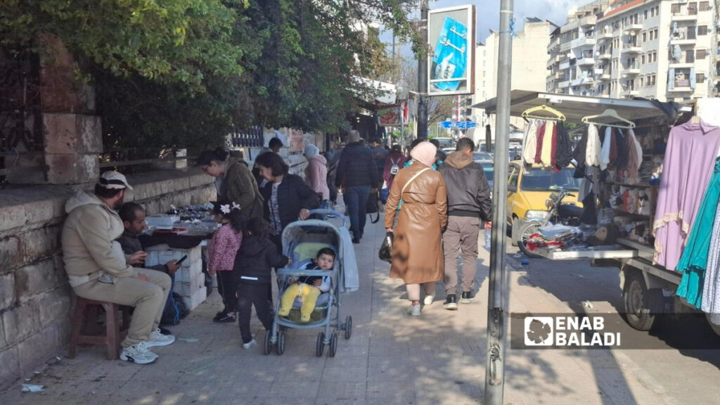 تنتشر البسطات على الأرصفة وفي محيط ساحة "الشيخ ضاهر" وسط مدينة اللاذقية ما يعوق حركة المشاة - 26 آذار 2026 (عنب بلدي)