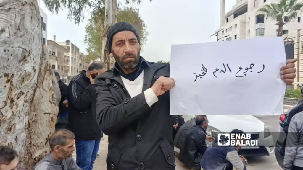 متظاهر في درعا يرفع لافتة احتجاجًا على قرار رفع الدعم عن الخبز - 15 نيسان 2026 (عنب بلدي/ محجوب الحشيش)