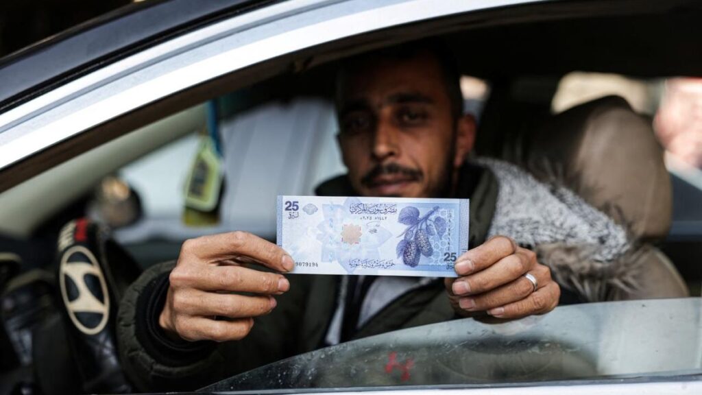 مواطن يحمل فئات من العملة السورية الجديدة (AFP)