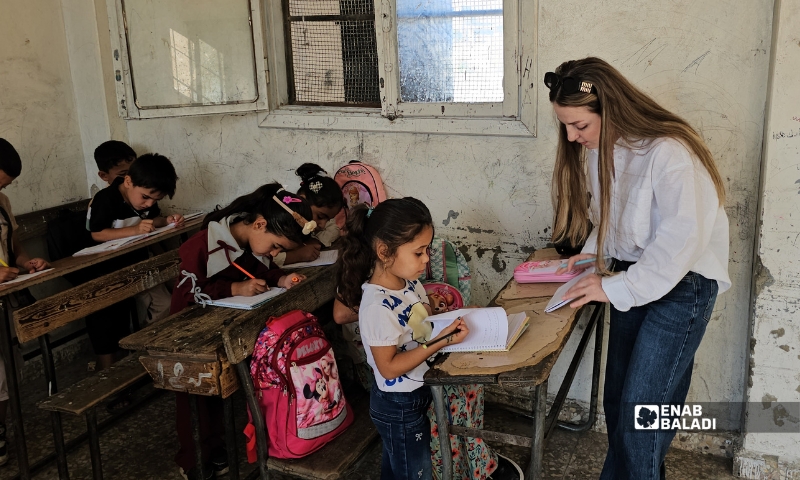 معلمة تتفقد دفاتر الطلاب الجدد في أحد الصفوف بمدرسة العزيزية في حماة مع انطلاق العام الدراسي - 6 أيلول 2026 (عنب بلدي)