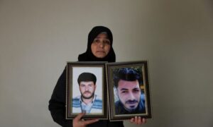 امرأة سورية تحمل صورة زوجها وشقيقها الذين فقد في معتقلات نظام الأسد - 23 تشرين الثاني 2025 (رويترز/خليل العشاوي)