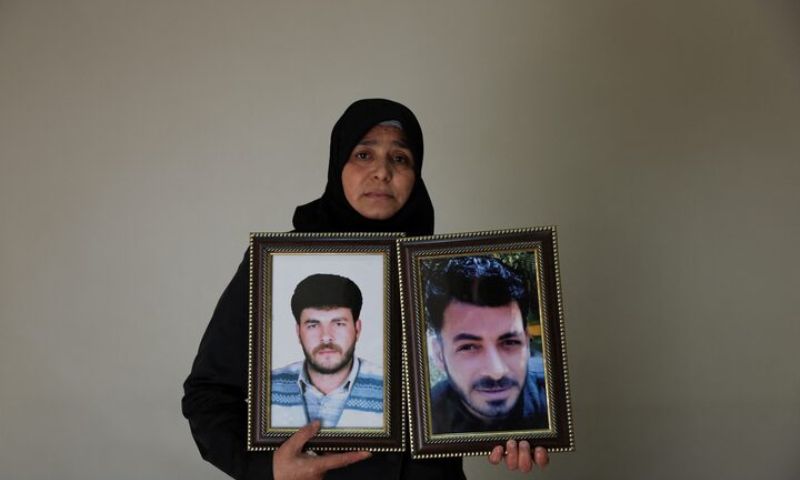 امرأة سورية تحمل صورة زوجها وشقيقها الذين فقد في معتقلات نظام الأسد - 23 تشرين الثاني 2025 (رويترز/خليل العشاوي)