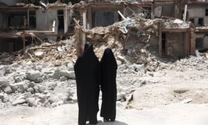امرأتان إيرانيتان تقفان أمام مبنى تضرر جراء غارة جوية -  22 آب 2026 (رويترز)