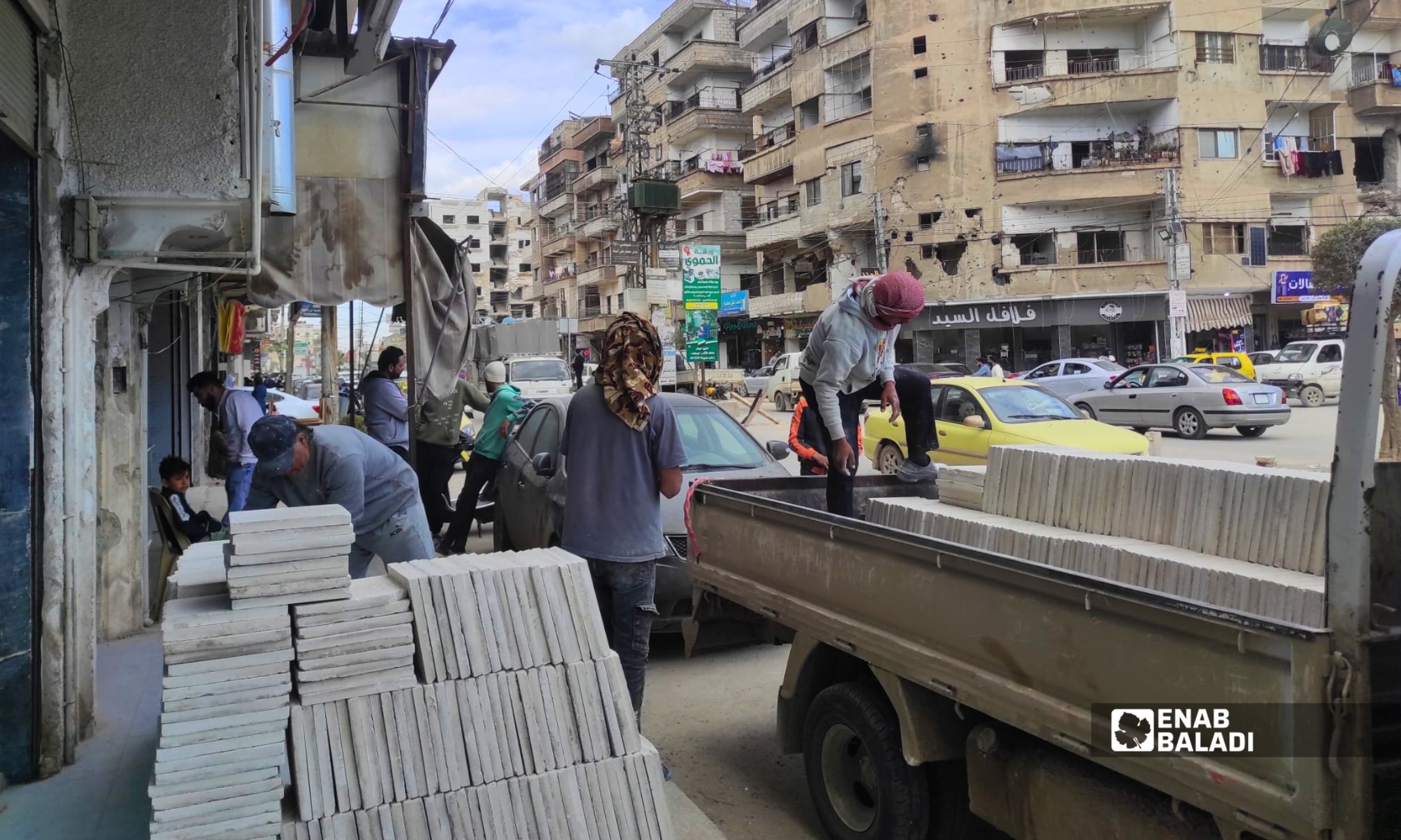 عمال يفرغون حمولة بلاط في محيط ساحة الترب بمدينة داريا