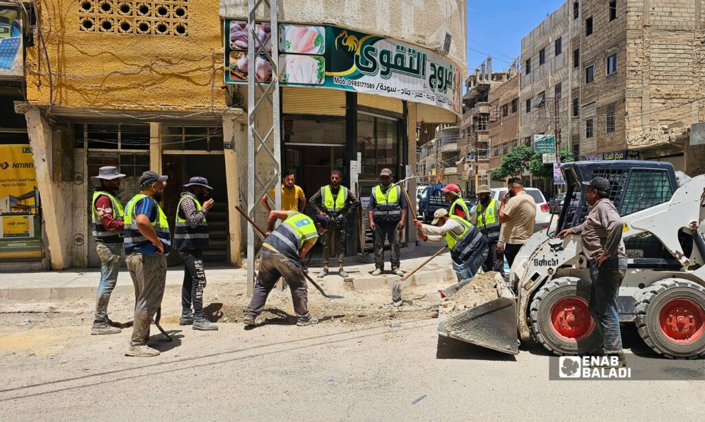 عمال يزفتون أحد المقاطع المحفورة في شارع الوحدة بمدينة داريا