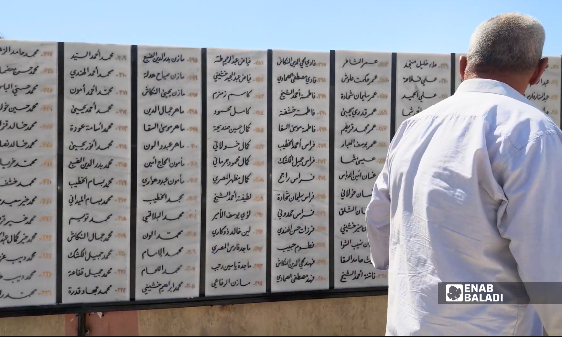أحد زوار جدارية ضحايا مجزرة داريا الكبرى يقف أمام الأسماء الموثقة