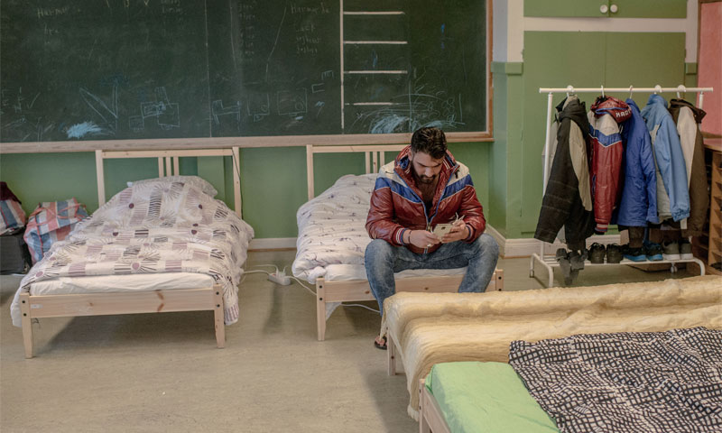 A Syrian refugee checking his phone in the asylum room in Sweden Camp, February 2016 (AFP)