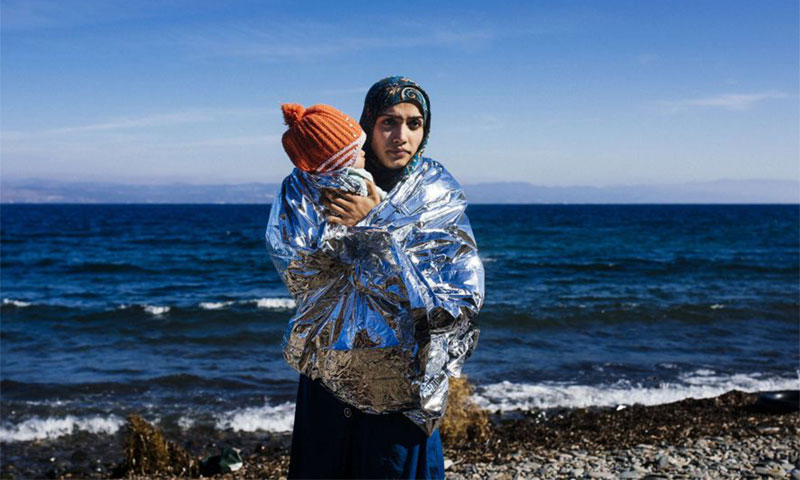 A Syrian refugee carrying her son as she arrives on Greek shores (EPA)