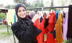 A woman from Homs, Syria, now a refugee in Lebanon, shows off knitted woolen clothes that she's learned how to make with support from the International Rescue Committee and UK aid. Photo by Russell Watkins/DFID