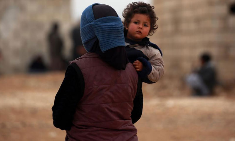 A Syrian woman displaced from Deir ez-Zor, carrying her child in a camp in Hasakah – February 26. 2018 (AFP)