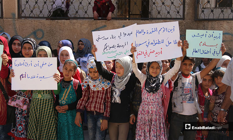 A protest organized by the educational staff of Kafr Oweid Town, rural Idlib, calling for the support of education in the liberated areas [Signs from left to right say: I have the right to see sweet dreams at sleep/ rebuild my school, destroyed by your missiles; my school is my second home/ Where are UN and the World in all that happened to childhood in Syria; my right to education/ I want to live in peace like the rest of the world’s children] – September 19, 2018 (Enab Baladi )