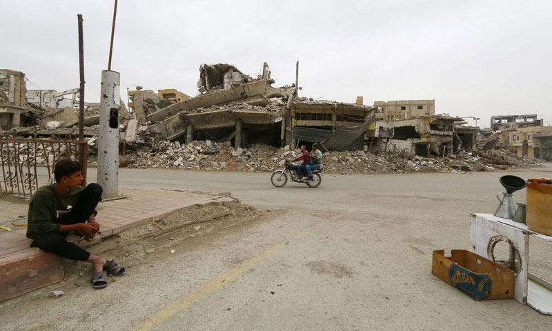 People riding motorcycles behind the destroyed buildings in Raqqa, Syria – October 12, 2018 (Reuters)