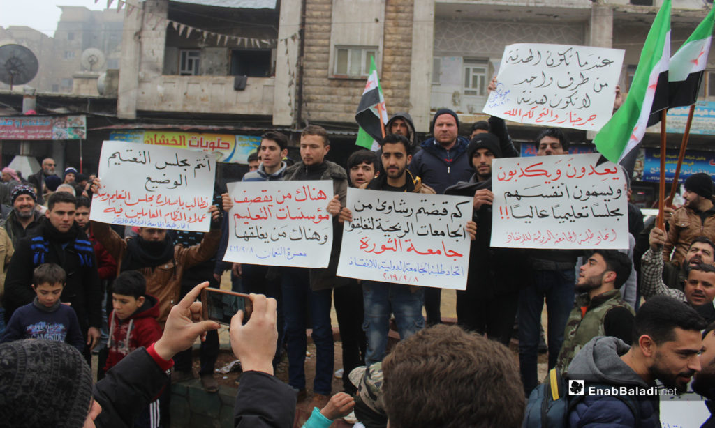 A demonstration in the city of Maarrat al-Nu'man protesting the decision of closing the International Rescue university in Idlib [From left to right the signs say: You are the Degraded Council of blackout; We want the Education Council Reformed and the Regime’s Agents Rebelled (Students Union of the International Rescue University). Some are Bombarding the Educational Institutions, Others are Closing them Down. How Much Have Your Received from Beneficial Universities to Shut Down that of the Revolution (Students Union of the International Rescue University). They Make You Promises and Lie to You, and They Dare Call Themselves a Higher Education Council (Students Union of the International Rescue University). A One-side truce is Not a Truce (Jarjanaz and al-Tah, God Is There for You!)]– February 8, 2019 (Enab Baladi)