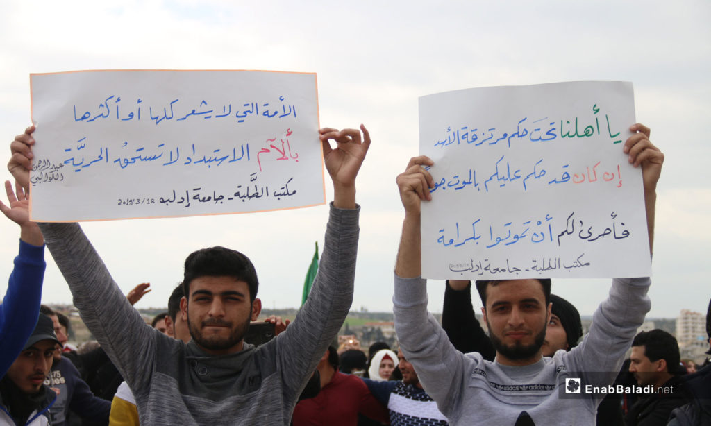 A demonstration by Idlib University students on the Syrian revolution’s eighth anniversary. The signs say: To our people under the power of Assad’s mercenaries-If you are sentenced to die of starvation-It is better that you die in dignity- Students Office, Idlib University/ "A nation, whose part and whole, does not feel the suffering of oppression is not worthy of freedom” Abd al-Rahman al-Kawakibi - Students Office, Idlib University – March 18, 2019 (Enab Baladi)