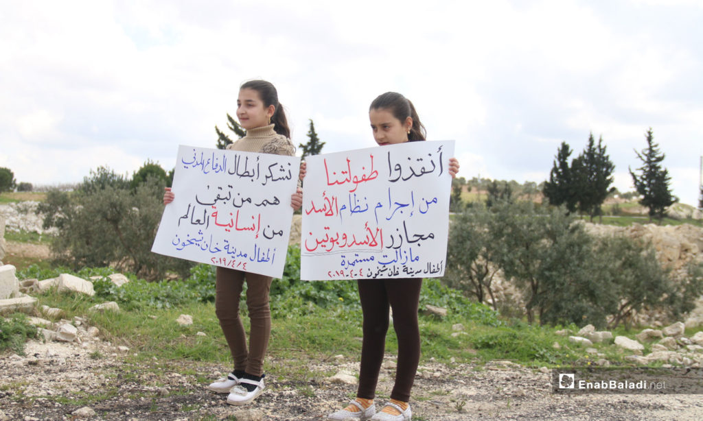A vigil at the second anniversary of the chemical massacre of Khan Shaykhun, rural Idlib – April 4, 2019 (Enab Baladi) The signs held by the two little girls say: “Save our childhood from the criminality of the al-Assad regime; Massacres by al-Assad and Putin are continuing/ We thank the heroes of the Civil Defense, they are what is left of the world’s humanity, the children of the city of Khan Shaykhun.”