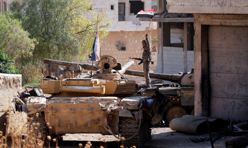 Soldier of the Syrian regime’s forces carrying up the ‘Syrian flag’ aboard a tank in Khan Shaykhun, rural Idlib – August 30, 2019 (Reuters)