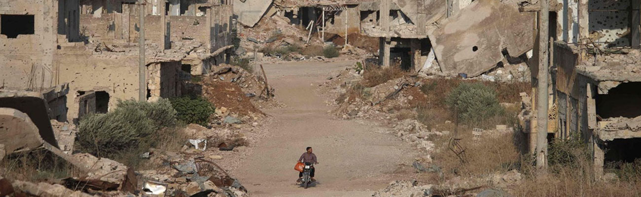 A man on his motorcycle behind him demolished buildings in southern city of Daraa - 2 August, 2018 (AFP) 