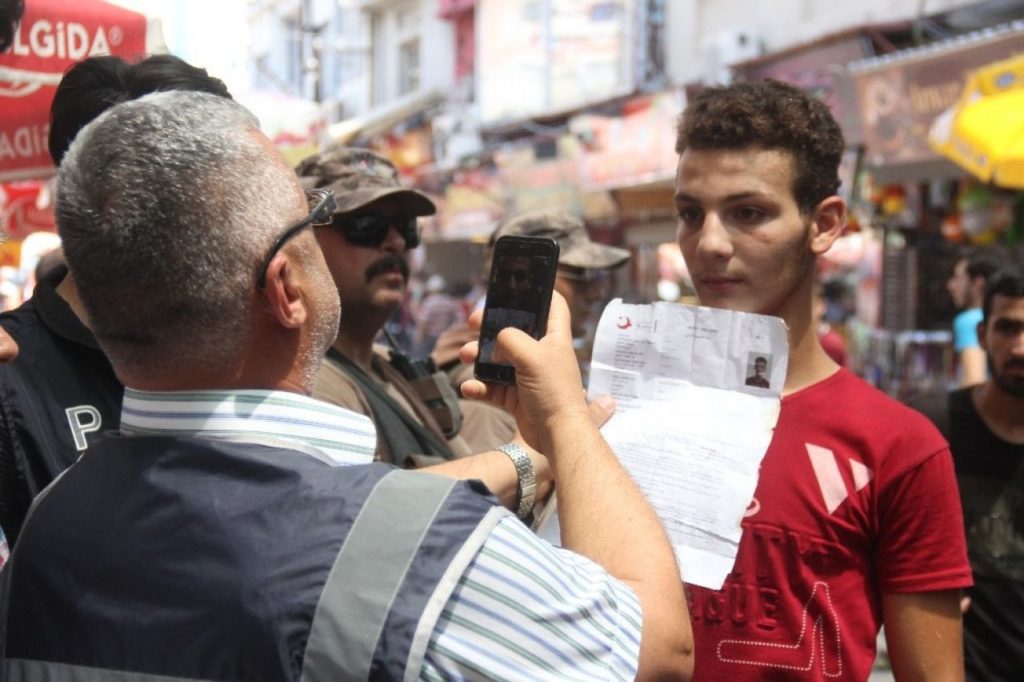 Turkish policeman taking a picture of a Syrian refugee using his mobile phone in Adana - July 10, 2019 (Taraf Medya)