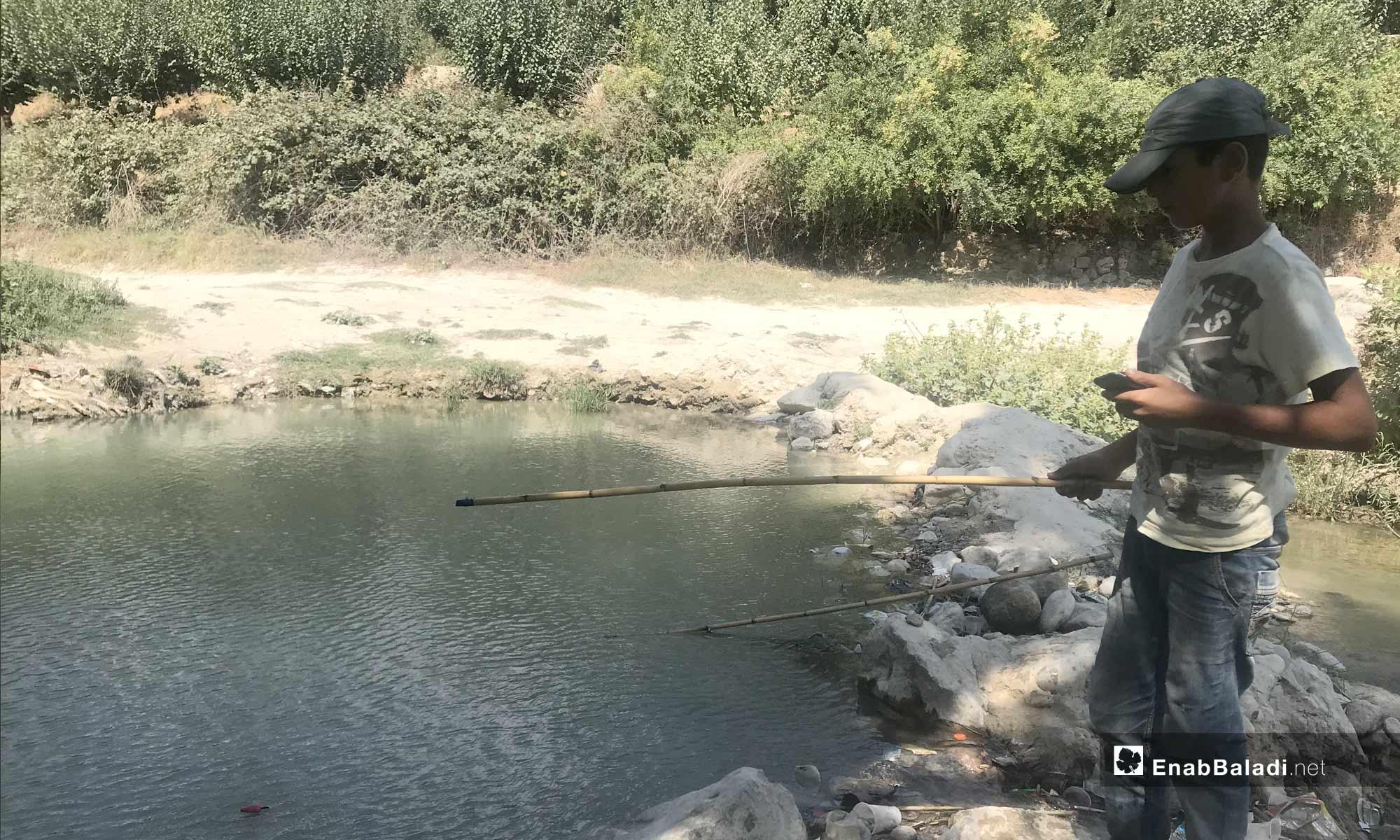 A young man fishing in the Assi River, near the city of Darkoush, western rural Idlib -September 8, 2019 (Enab Baladi)