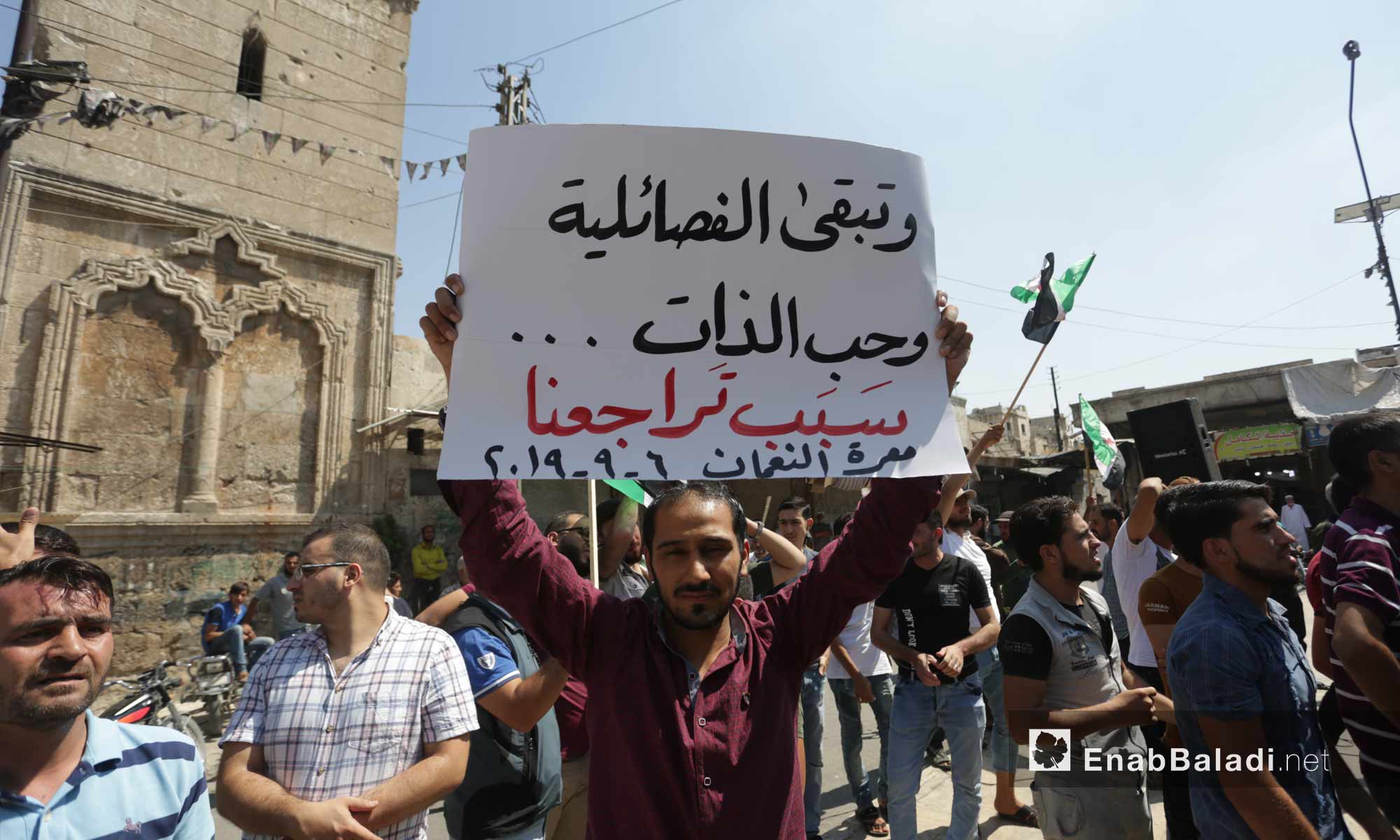 People in Ma`arat al-Nu`man, rural Idlib, protesting against the Sochi deal and demanding the ousting of the Syrian regime. One of the people holding a sign, saying: “Factionalism and egoism will always be the reason for our retreat” – September 6, 2019 (Enab Baladi)