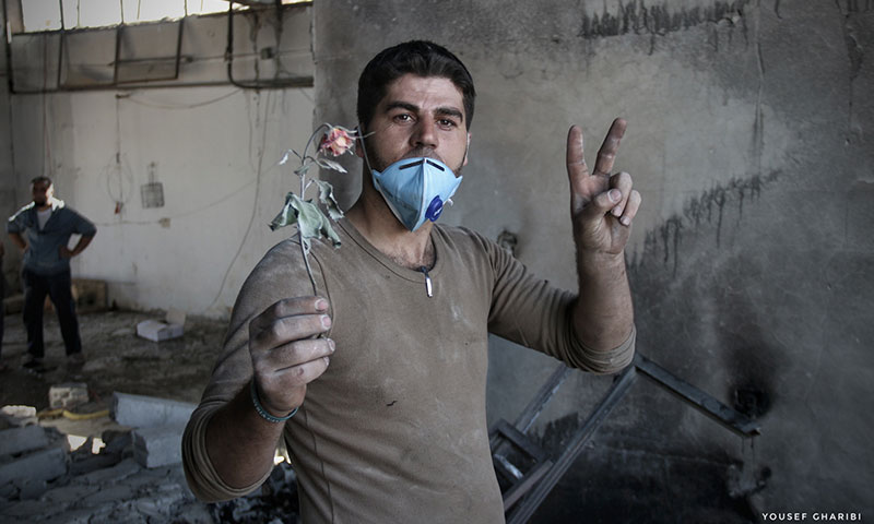 A member of the Syrian Civil Defense (also known as the White Helmets), holding a rose at the entrance of a bombed center in the village of Kafr Nabl, in southern Idlib. (Yousef Ghraibi)