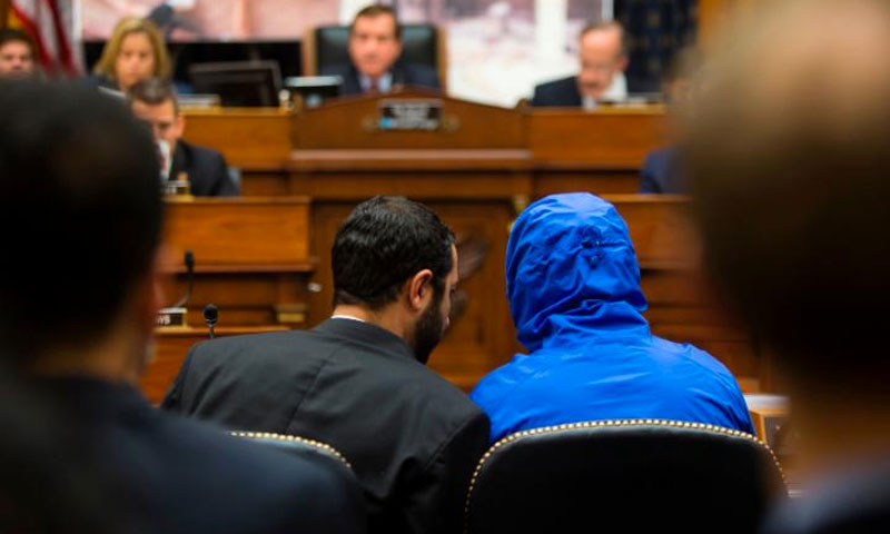 Syrian defector Caesar conceals his identity as he listens with a translator to the House Foreign Affairs Committee in 2014 (CNN)