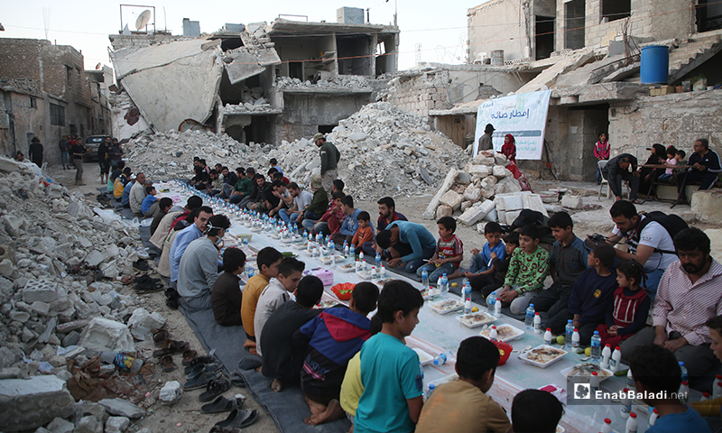 Residents of Atarib city in rural Aleppo gathering for a public iftar, surrounded by grey destruction and rubble - 8 May 2020 (Enab Baladi)
