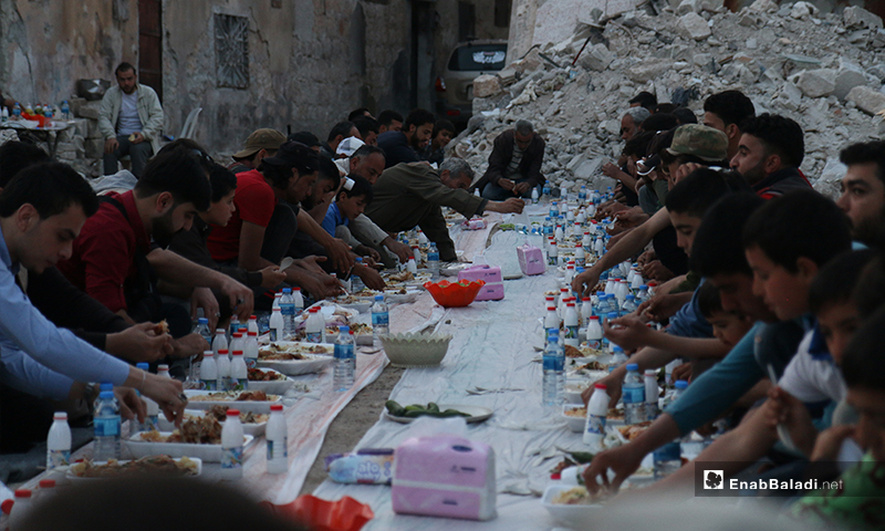 Residents of Atarib city in rural Aleppo gathering for a public iftar, surrounded by grey destruction and rubble - 8 May 2020 (Enab Baladi)

