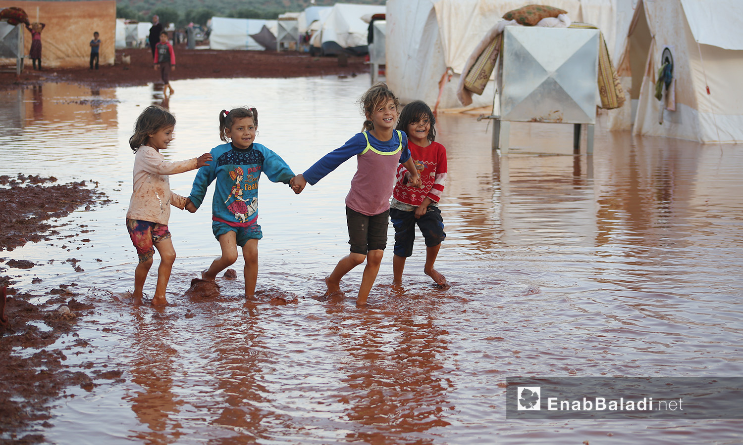 Children playing in the stormwater after the rainstorm that hit “Sahl al-Khair” camp for Syrian internally displaced people (IDPs) near Kafr Bunni in northern Idlib countryside – 19 June 2020  (Enab Baladi / Yousef Ghuraibi)
