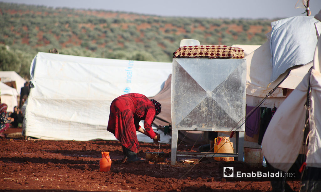 A woman washing dishes at “Sahl al-Khair” camp for Syrian internally displaced people (IDPs) after the rainstorm near Kafr Bunni in northern Idlib countryside – 19 June 2020 (Enab Baladi / Yousef Ghuraibi)