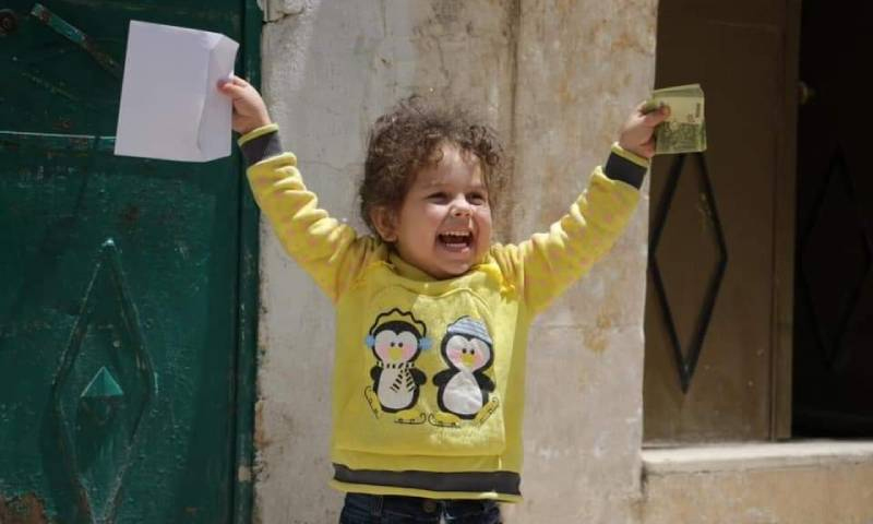 A Syrian child is extremely happy to receive eidi on the first day of Eid al-Fitre- 2020 (Molhman Volunteering Team)