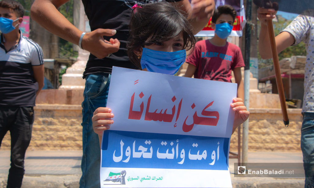 A child holding a sign at a protest stand in Idlib city’s Clock Square – 10 July 2020 (Enab Baladi / Anas al-Khouli)