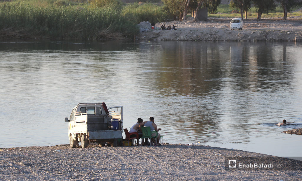 Young men sitting on the Euphrates River's bank in al-Raqqa province – 24 July 2020 (Enab Baladi / Abdul Aziz Saleh)